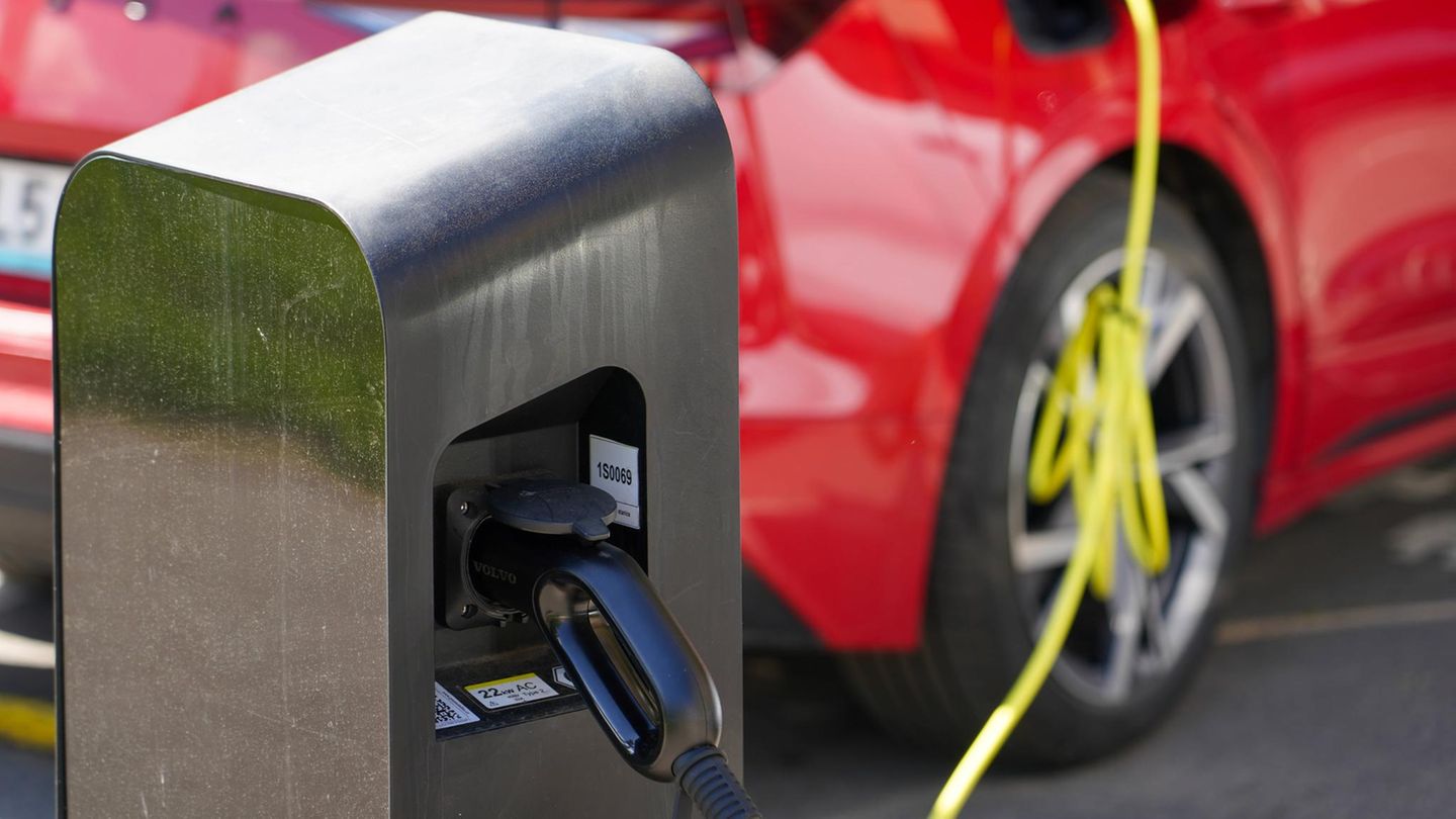 Symbolbild: Rotes Plug-in-Hybrid-Auto im Hintergrund unscharf angeschlossen an der Zapfsäule im Vordergrund