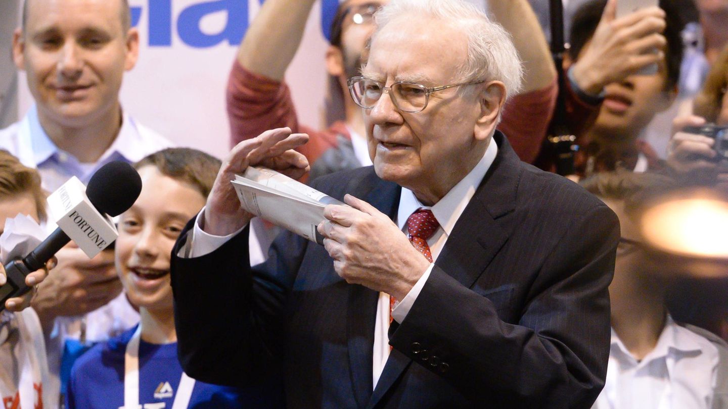 Warren Buffett mit Zeitung in der Hand, umgeben von Repotern