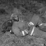 Ein Feuerwehrmann liegt im Gras auf seinem Rucksack, er schaut direkt in die Kamera