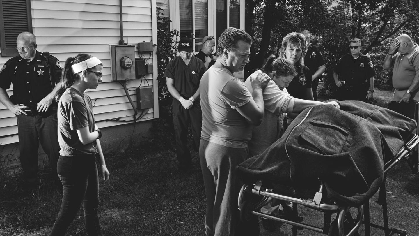 Eine eindrucksvolle Fotografie, wo eine Familie und Beamte um eine Trage mit einem Leichensack stehen