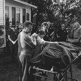 Eine eindrucksvolle Fotografie, wo eine Familie und Beamte um eine Trage mit einem Leichensack stehen