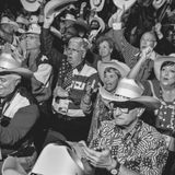 EIne Gruppe weißer Amerikaner in Cowboyhüten und Kleidung mit USA-Flagge freuen sich, strecken Arme hoch, sie gröhlen