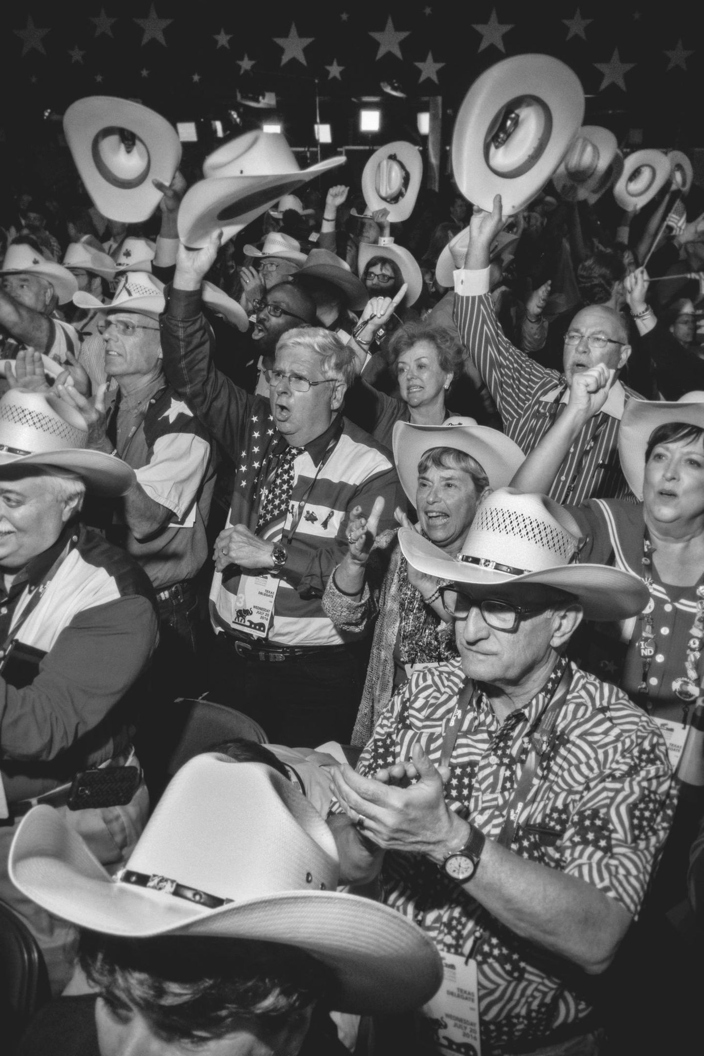 EIne Gruppe weißer Amerikaner in Cowboyhüten und Kleidung mit USA-Flagge freuen sich, strecken Arme hoch, sie gröhlen