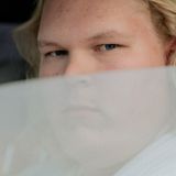 Junger Mann blickt aus seinem halbgeöffneten Autofenster in die Kamera.