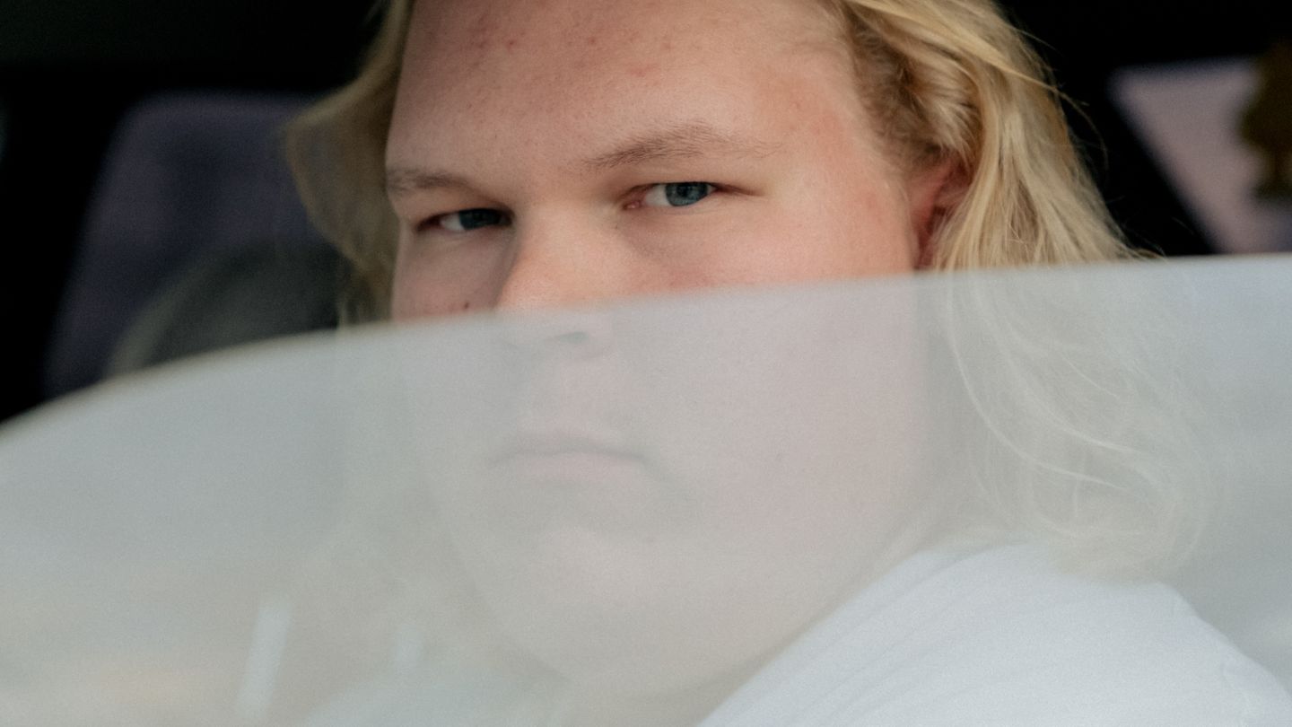 Junger Mann blickt aus seinem halbgeöffneten Autofenster in die Kamera.