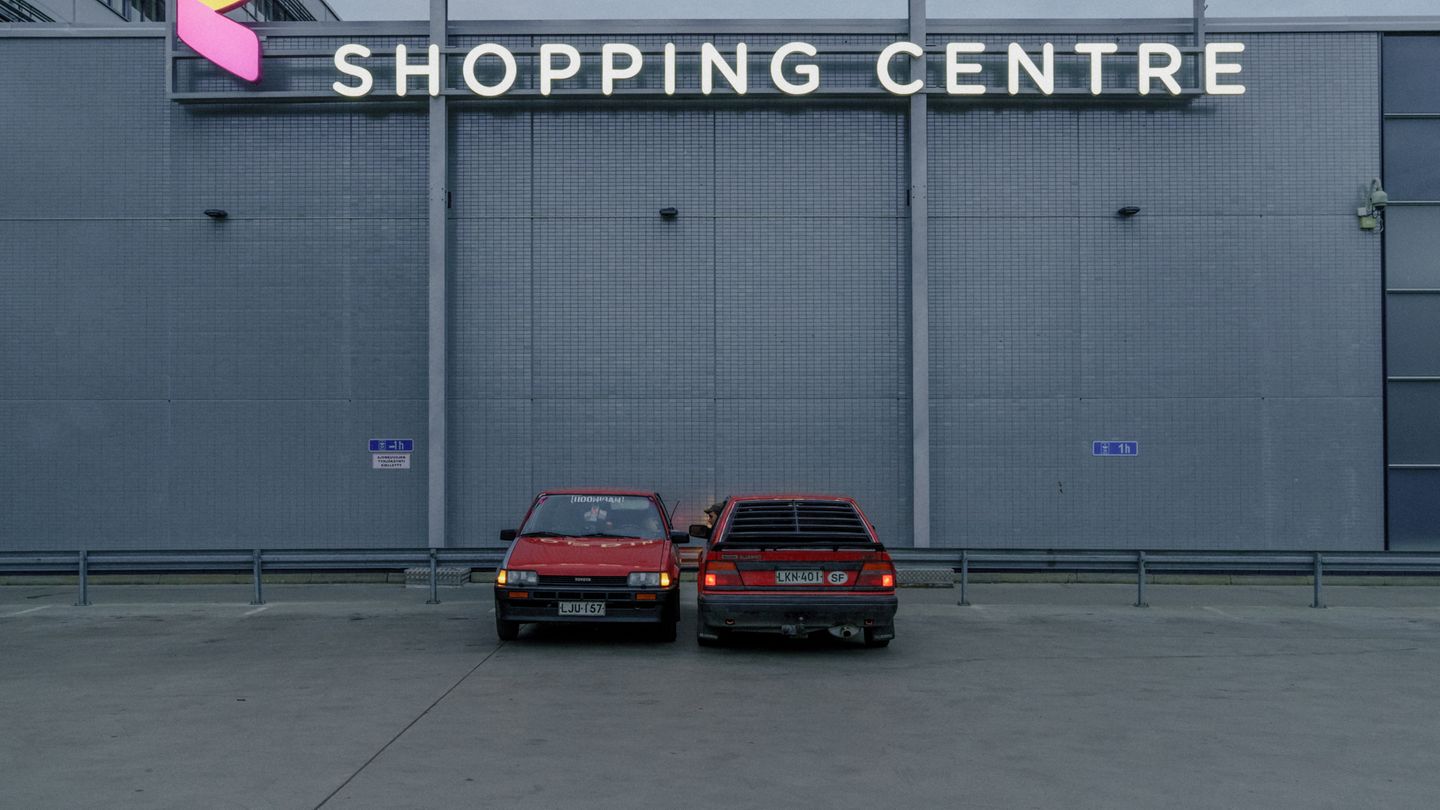 Zwei rote Autos stehen auf dem Parkplatz vor einem Shopping Center.