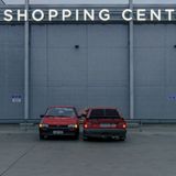 Zwei rote Autos stehen auf dem Parkplatz vor einem Shopping Center.