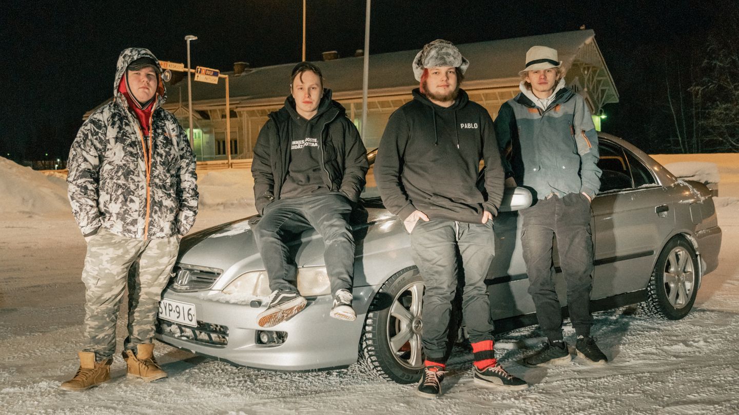 Vier junge Männer posieren im Schnee vor einem alten Honda