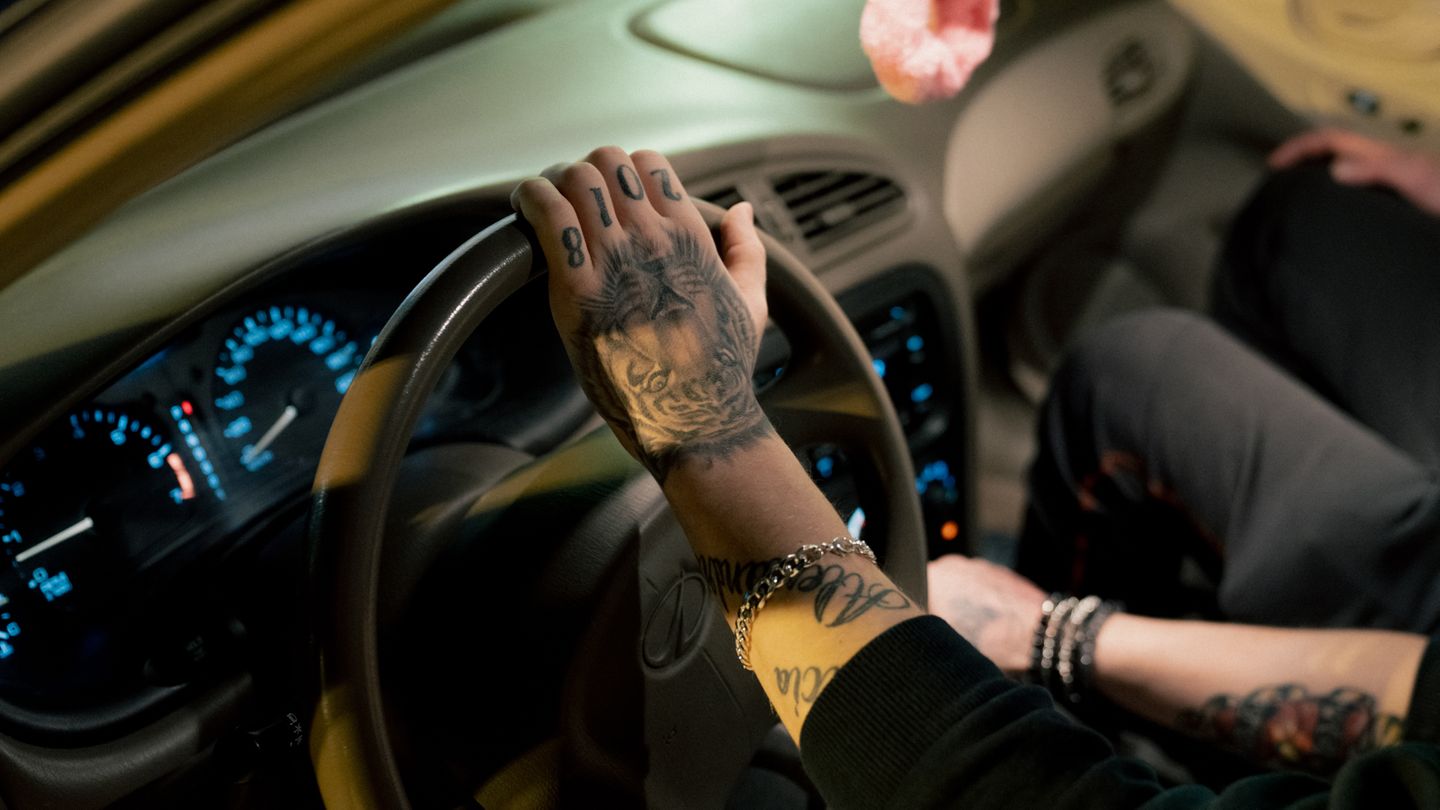 Detailaufnahme von dem Arm eines Autofahrers, der ein Löwen-Tatoo und die Zahl 2018 auf der Hand tättowiert hat.