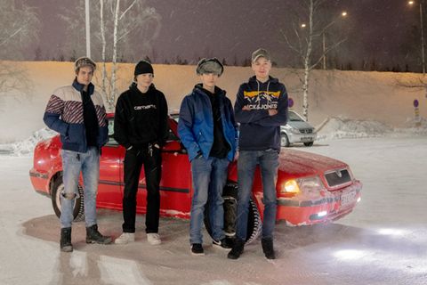 Vier männliche Jugendliche aus Finnland stehen vor einem roten Auto auf einem verschneiten Parkplatz.