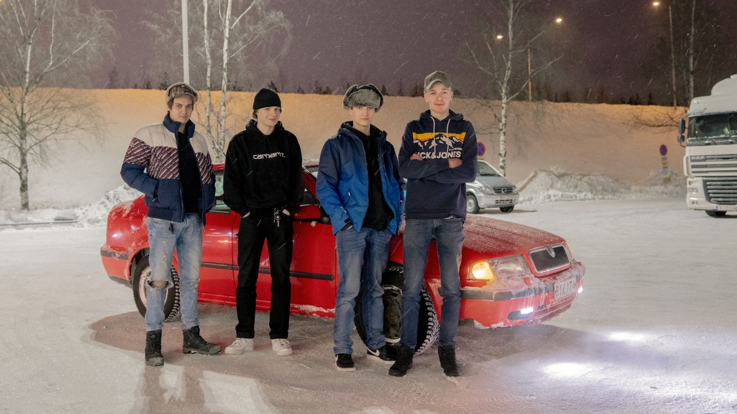 Vier männliche Jugendliche aus Finnland stehen vor einem roten Auto auf einem verschneiten Parkplatz.