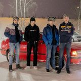 Vier männliche Jugendliche aus Finnland stehen vor einem roten Auto auf einem verschneiten Parkplatz.