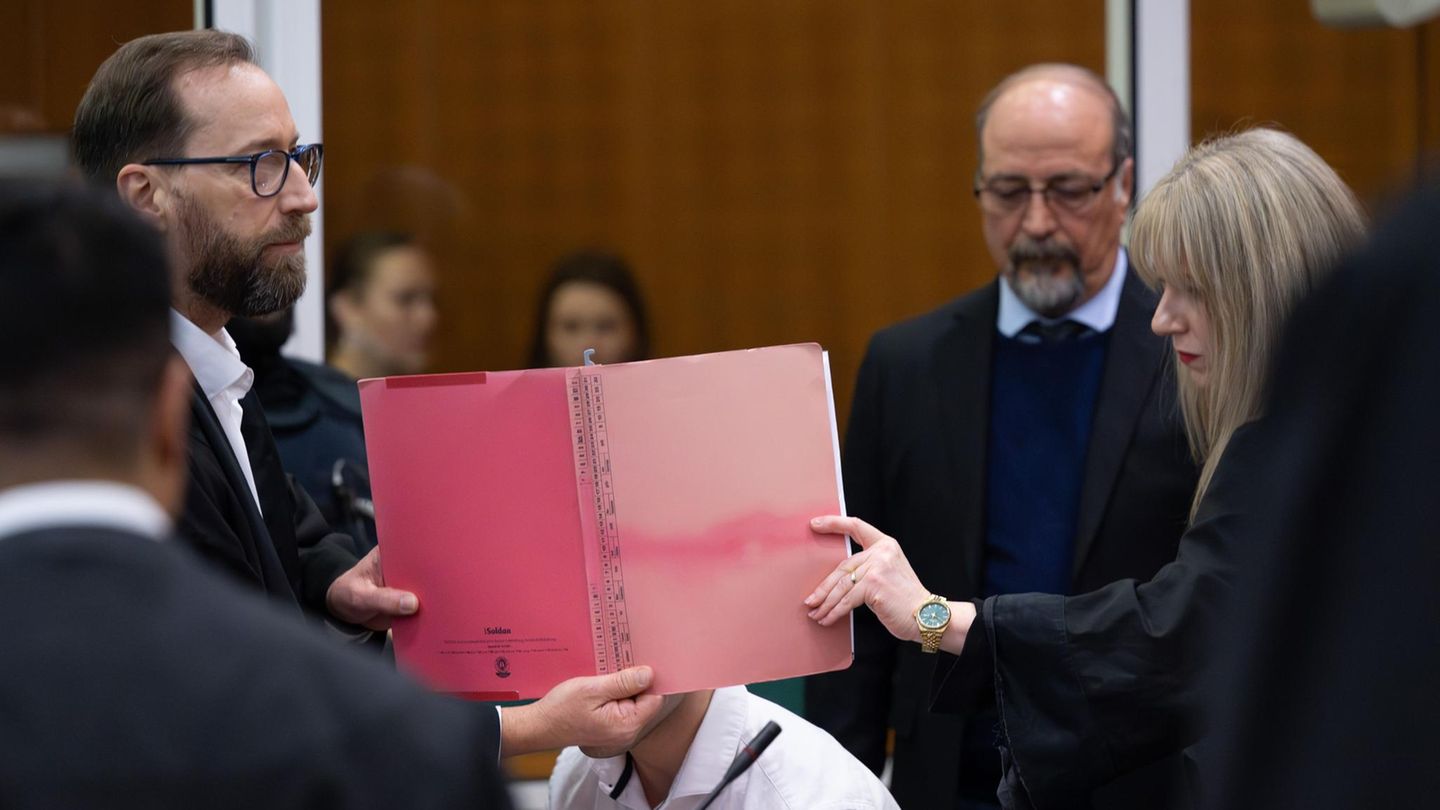 Anwälte von einem der acht Angeklagten halten ihrem Mandanten eine Akte vors Gesicht, um ihn von den Kameras abzuschirmen