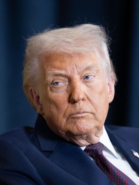 Donald Trump sitzt in einem blauen Anzug vor einem Blauen Vorhang und schaut unzufrieden