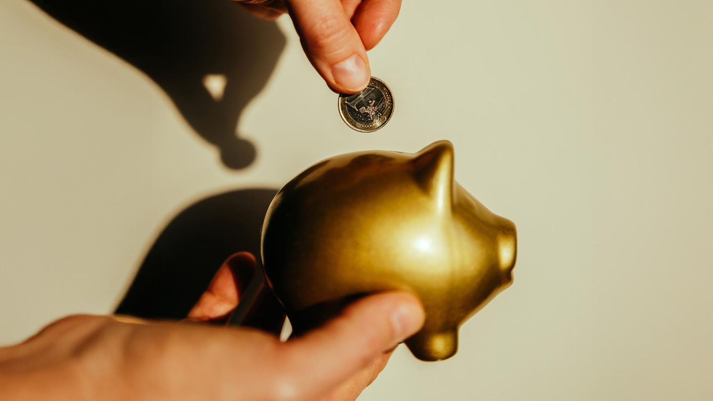 Hände werfen einen Euro in ein goldenes Sparschwein