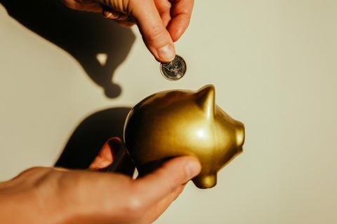 Hände werfen einen Euro in ein goldenes Sparschwein