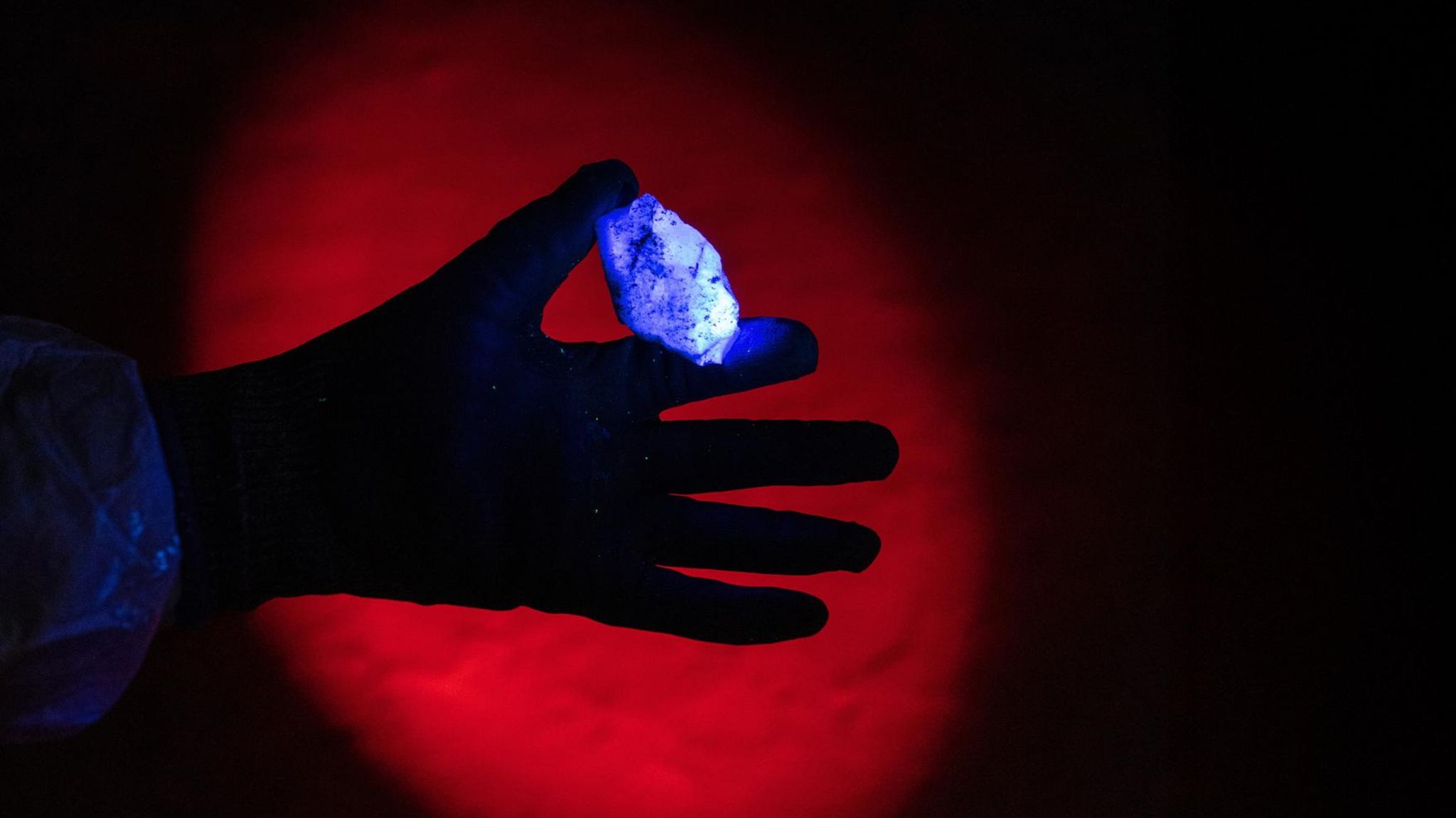 Eine Hand hält einen blau leuchtenden Fluoritkristall