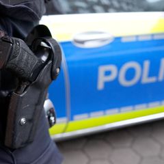 Polizist mit Waffe vor einem Polizeiauto, Symbolbild Messerangriff Böhl-Iggelheim