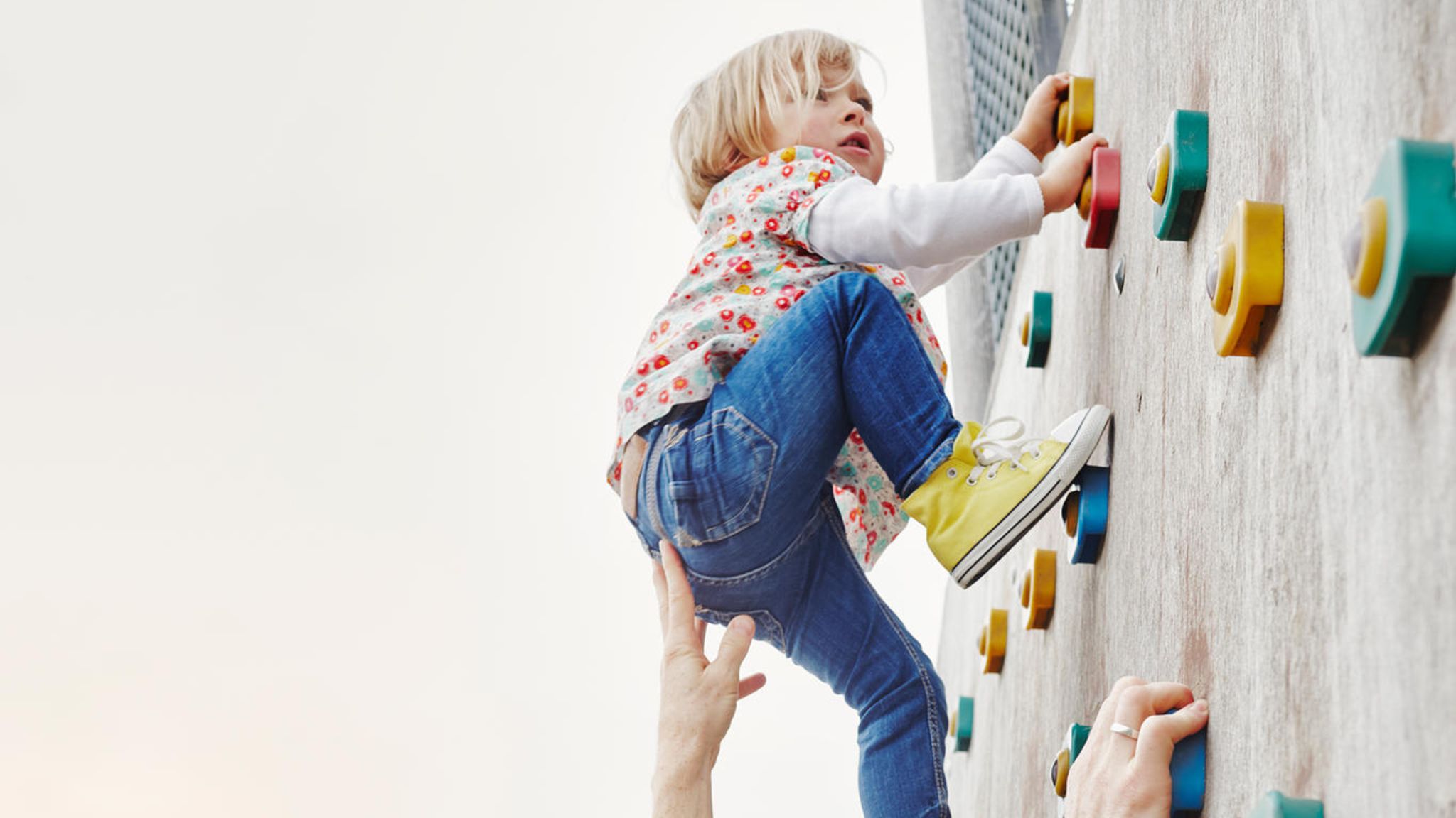 Vater hilf Tochter beim Klettern an Kletterwand