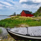 Im Vordergrund ein Holzboot, im Hintergrund ein rotes Holzhaus an einem See gelegen