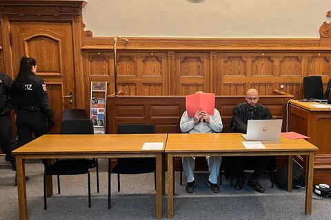 Ein Mann hält sich einen Aktenordner vors Gesicht / Prozessauftakt Ehrenmord