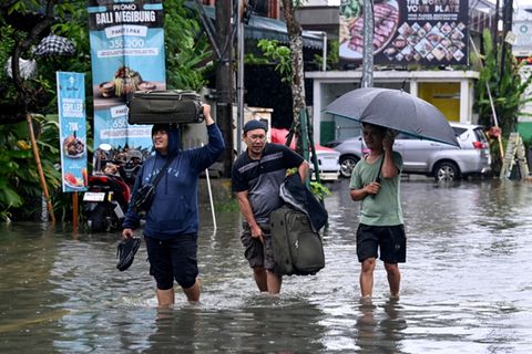 Hotelgäste auf Bali tragen ihr Gepäck durch die überfluteten Straßen