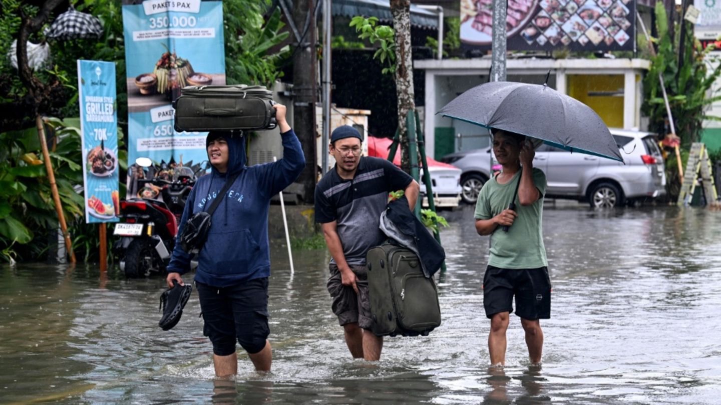 Hotelgäste auf Bali tragen ihr Gepäck durch die überfluteten Straßen