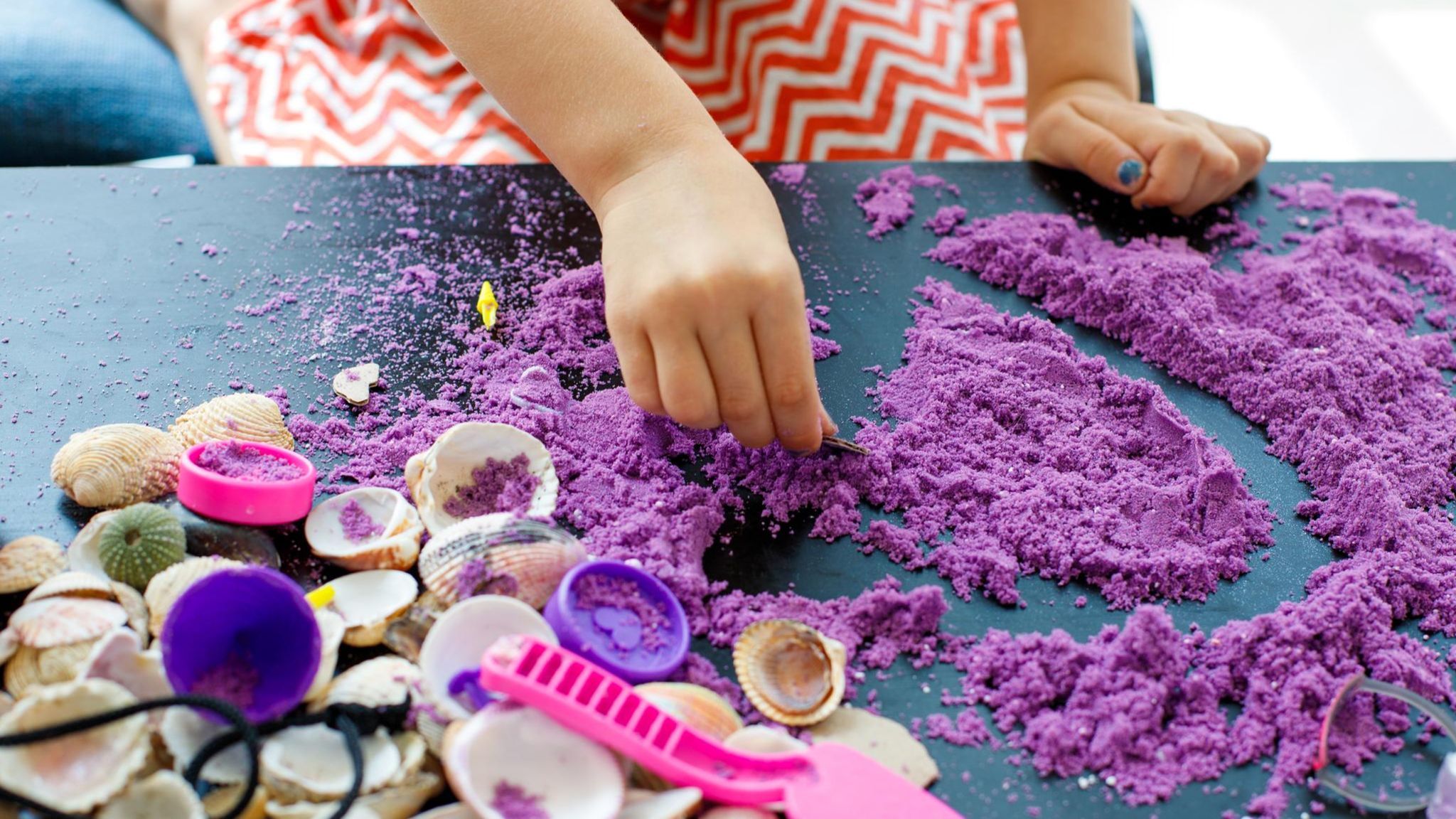 Spielzeug: Ein Kind spielt mit farbigem Sand