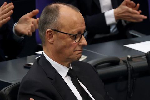 Friedrich Merz sitzt im Plenarsaal des Deutschen Bundestages, während die Abgeordneten um ihn herum applaudieren