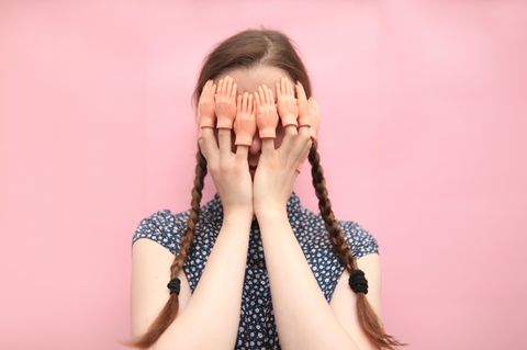 Eine Frau hält sich die Hände vor das Gesicht. Auf den Fingern sitzen jeweils kleine Aufsteck-Hände