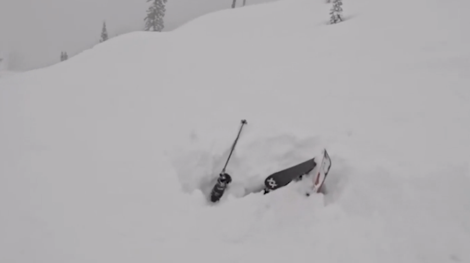 Eine Person ist mit ihren Skiern unter Schnee begraben.