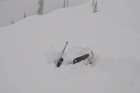 Eine Person ist mit ihren Skiern unter Schnee begraben.