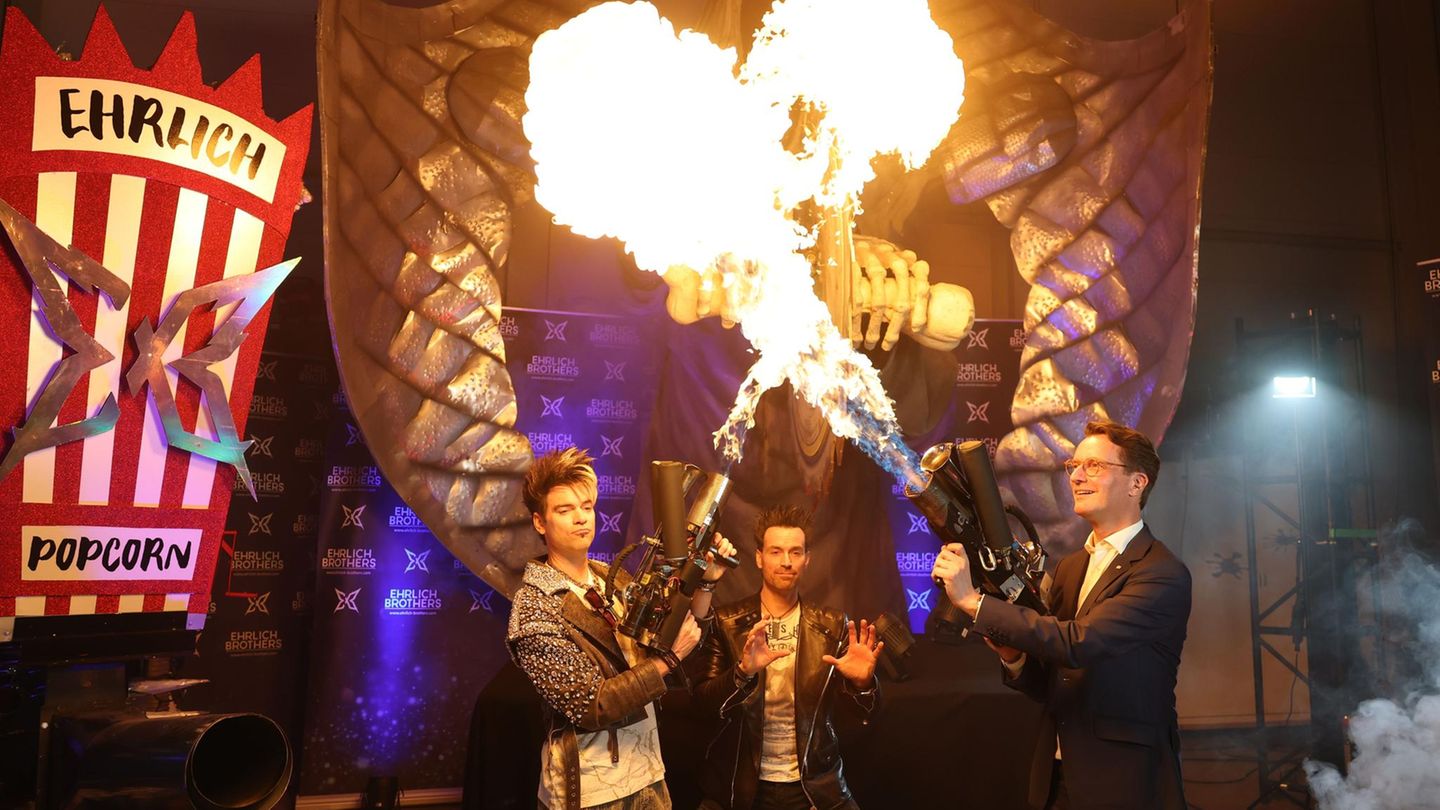 Bünde, Deutschland. Hendrik Wüst (r.) ist Feuer und Flamme: Auf seiner Ostwestfalen-Tour besucht der Ministerpräsident von Nordrhein-Westfalen den Firmensitz des Zauberer-Duos „Ehrlich Brothers“. Die Brüder Chris (l.) und Andreas (M.) zeigen dem CDU-Politiker dabei, wie man mit einem Flammenwerfer umgeht.