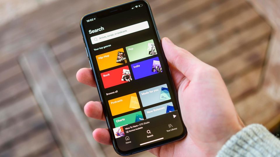 Eine Hand hält ein Handy, auf dem die Spotify-App geöffnet ist