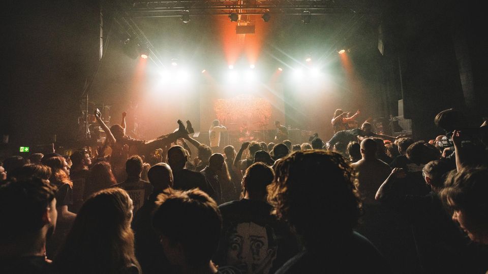 Eine kleine Menschenmenge steht vor einer Bühne und jubelt einer Band zu