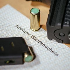 Ein Kleiner Waffenschein liegt zwischen einer Schreckschuss-Pistole, einem Magazin und einer Knallpatrone