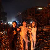 Drei junge Leute laufen bei Nacht in Pyjamas auf einer zerstörten Straße. Sie sind staubbedeckt.