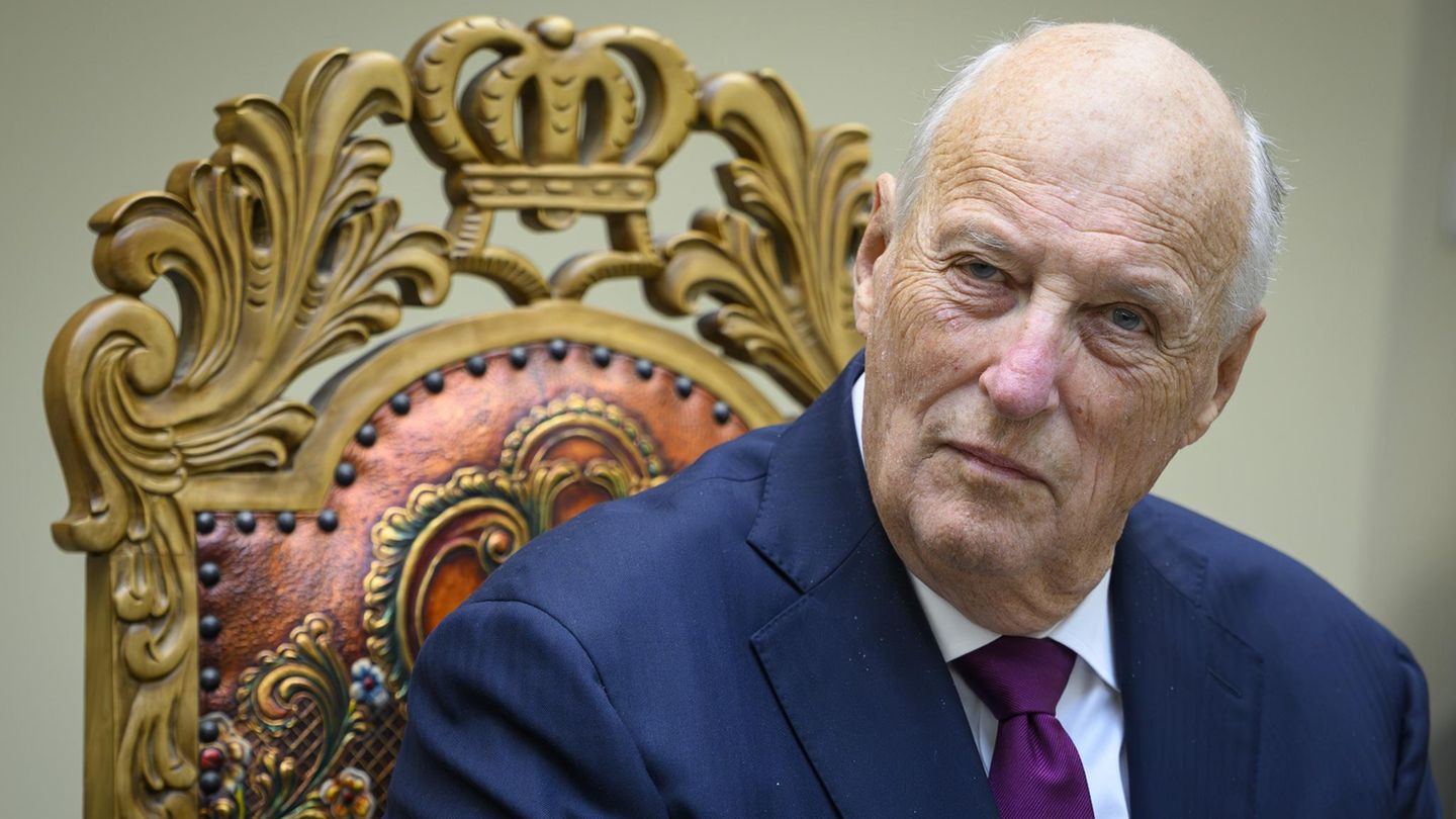König Harald V. von Norwegen sitzt auf einem Stuhl und blickt in die Kamera