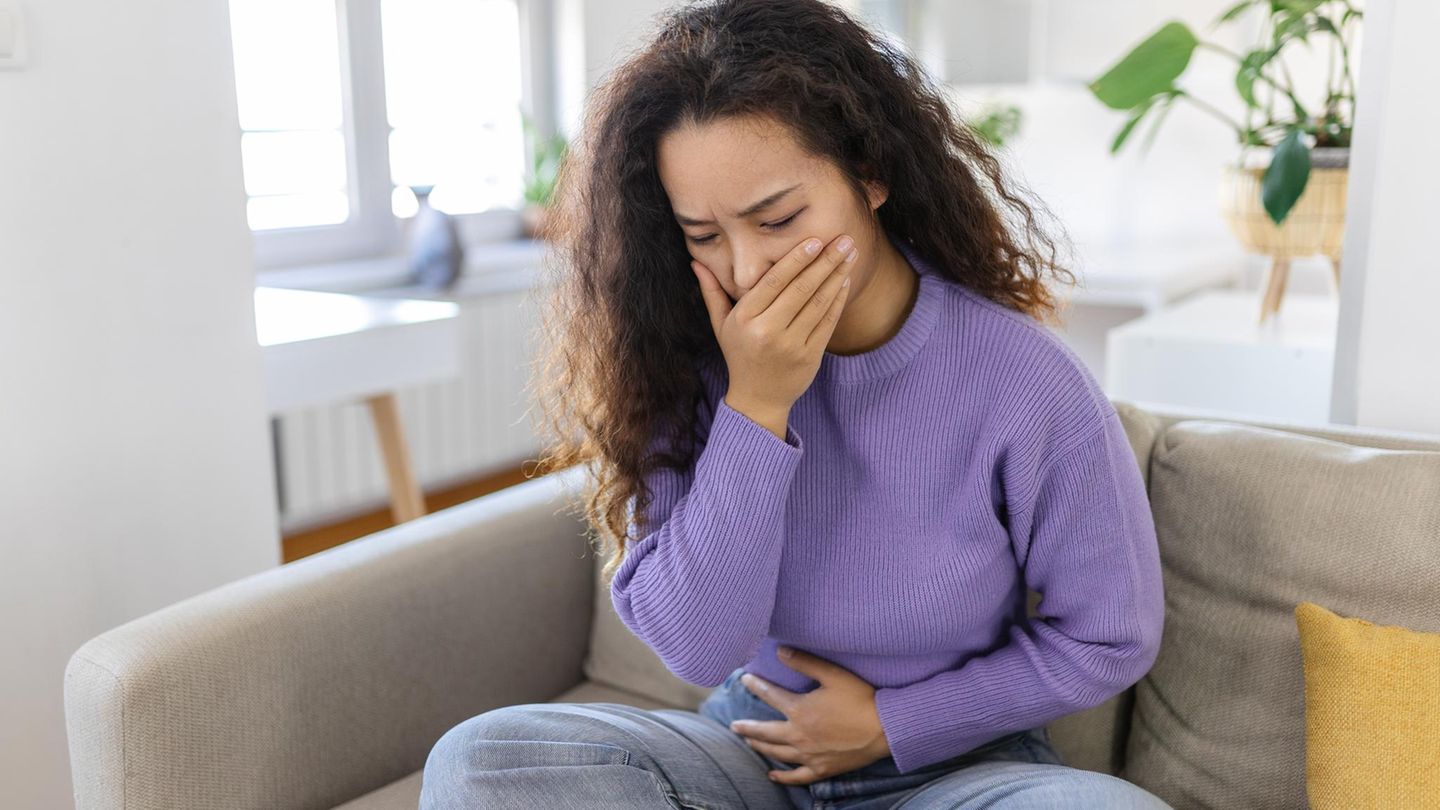 Angst vor dem Erbrechen: junge Frau sitzt mit Hand vor dem Mund auf dem Sofa
