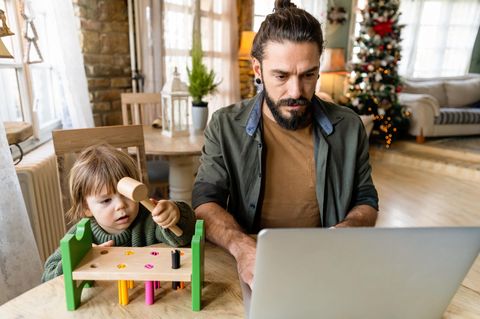 Mann arbeitet am Laptop, neben ihm ein Kind