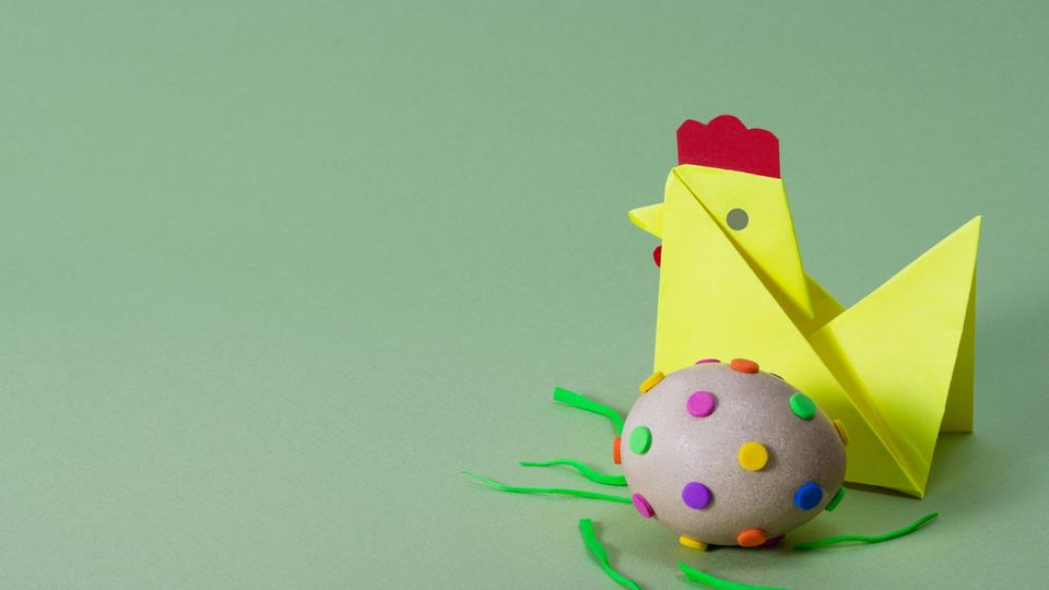 Ein gelbes, aus Origami-Papier gefaltetes Küken vor grünem Hintergrund