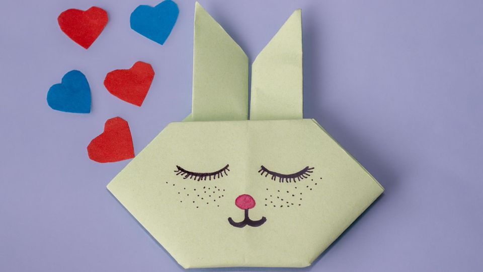 Ein grüner Origami-Hase mit pinker Nase vor lila Hintergrund