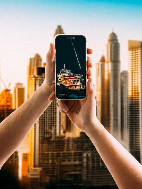 Hände halten ein Smartphone vor der Skyline von Dubai