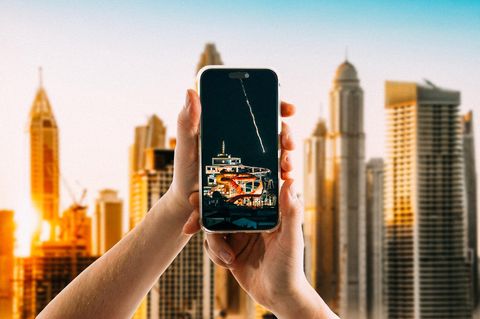 Hände halten ein Smartphone vor der Skyline von Dubai