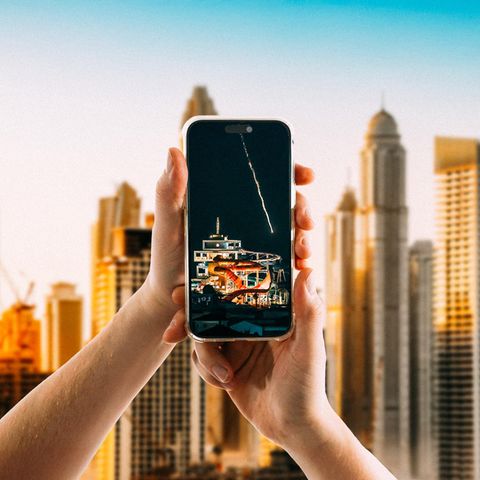 Hände halten ein Smartphone vor der Skyline von Dubai
