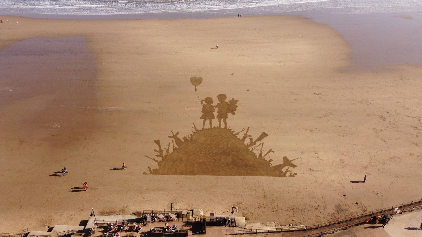 Scarborough, England. Ein Künstler namens Fred Brown huldigt dem britischen Streetart-Künstler Banksy, indem er dessen ikonisches Kunstwerk „Kids on Guns” aus dem Jahr 2003 am Strand nachahmt. Brown nutzte eine Harke, um eine riesige Version des berühmten Werks im Sand zu skizzieren. Besonders auf Luftaufnahmen wie dieser sieht es beeindruckend aus. Die Sandversion erschien nach den jüngsten US-israelischen Angriffen auf den Iran.