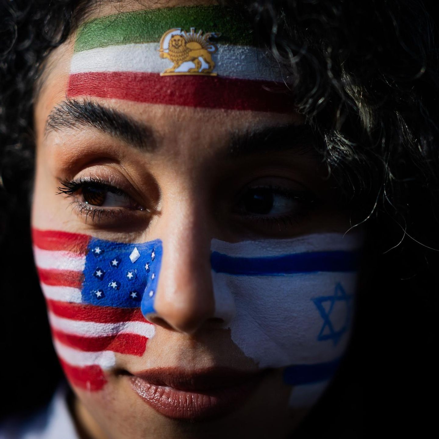 Berlin, Deutschland. Mozhgan nimmt mit den auf das Gesicht gemalten Flaggen der USA, Israels und des Irans an einem Protest unter dem Motto „Feiern des getöteten Diktators des Iran“ am Brandenburger Tor teil. Hunderte Menschen haben bei der Kundgebung am Brandenburger Tor Freiheit für den Iran gefordert. Redner erinnerten an die Tausenden Menschen, die während der Proteste zu Beginn des Jahres im Iran ermordet wurden, und an die Tausenden, die noch gefangen gehalten werden. Viele Teilnehmer der Kundgebung schwenkten iranische Fahnen. Vor der Bühne hingen auch eine deutsche, eine israelische und eine amerikanische Flagge.