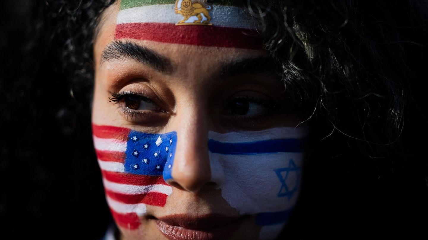 Berlin, Deutschland. Mozhgan nimmt mit den auf das Gesicht gemalten Flaggen der USA, Israels und des Irans an einem Protest unter dem Motto „Feiern des getöteten Diktators des Iran“ am Brandenburger Tor teil. Hunderte Menschen haben bei der Kundgebung am Brandenburger Tor Freiheit für den Iran gefordert. Redner erinnerten an die Tausenden Menschen, die während der Proteste zu Beginn des Jahres im Iran ermordet wurden, und an die Tausenden, die noch gefangen gehalten werden. Viele Teilnehmer der Kundgebung schwenkten iranische Fahnen. Vor der Bühne hingen auch eine deutsche, eine israelische und eine amerikanische Flagge.