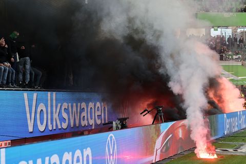 Fans von Wolfsburg werfen Leuchtfackeln auf den Platz. Foto: Andreas Gora/dpa