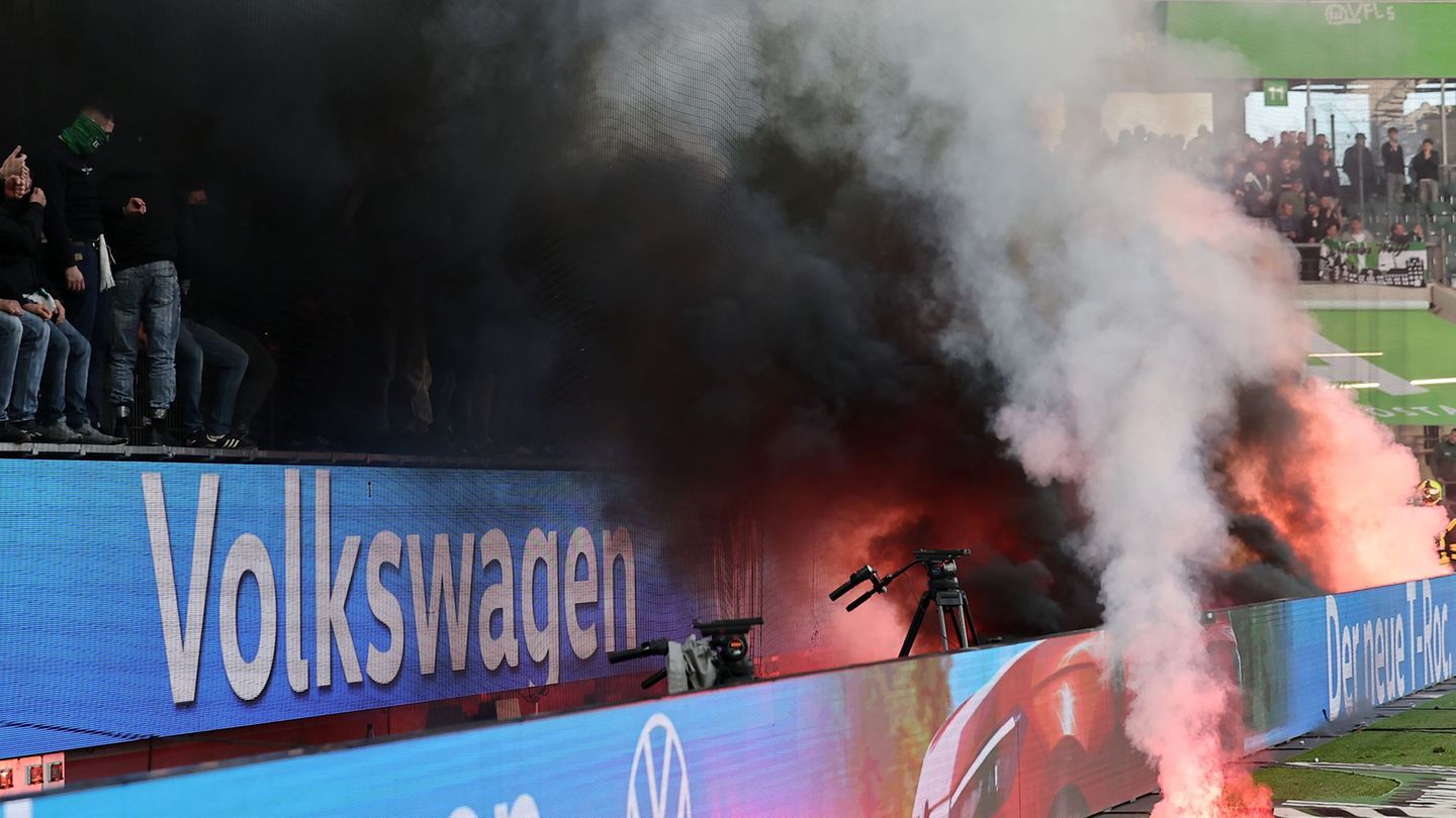 Fans von Wolfsburg werfen Leuchtfackeln auf den Platz. Foto: Andreas Gora/dpa